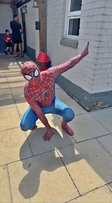 Spider-Man mid-action pose outside a venue with a family in the background